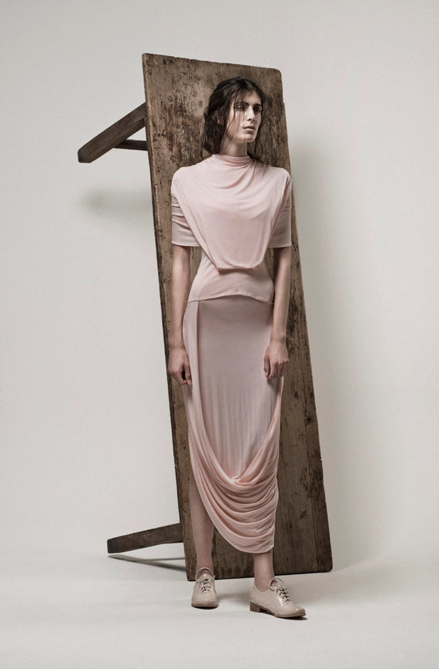 Woman  model wearing a flowing pink outfit standing against a table