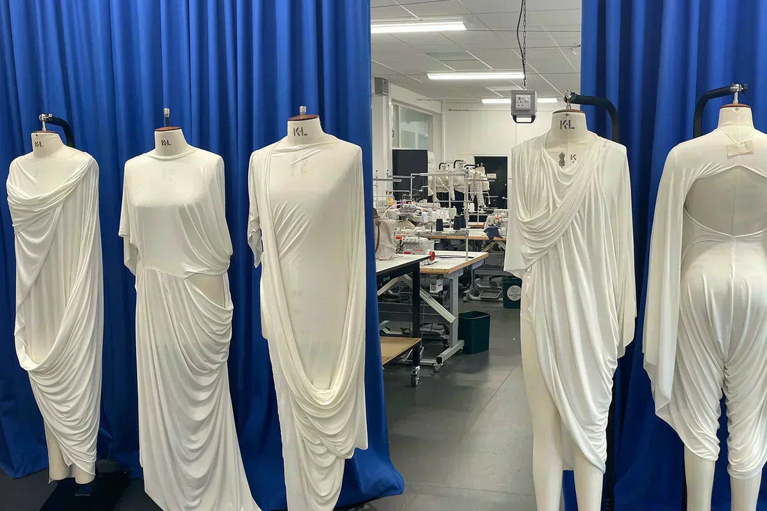 A row of mannequins in a line wearing white zero waste sustainable fashion in front of a blue curtain