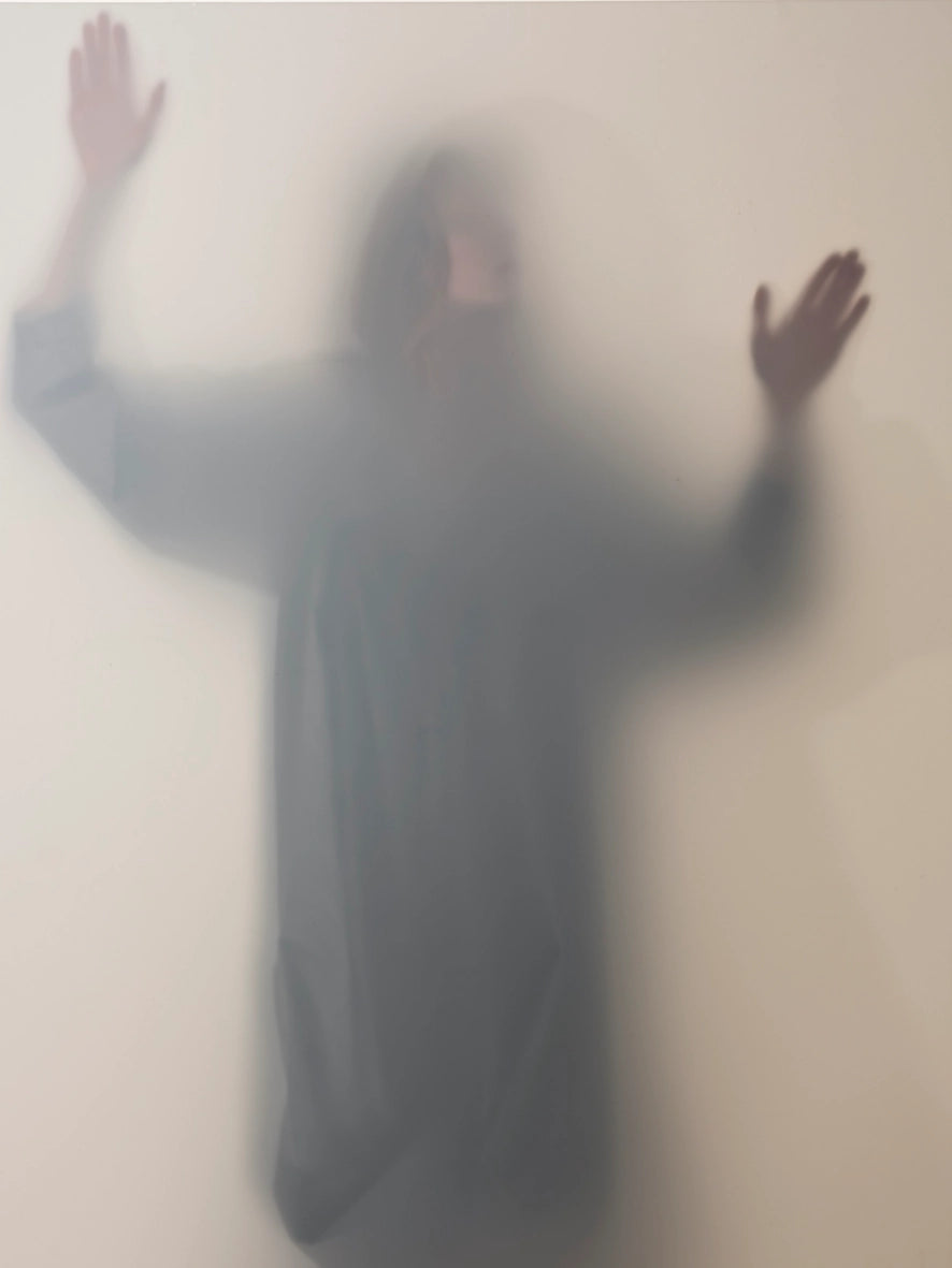 Person wearing luxury dress by cunnington & sanderson with arms outstretched against a foggy glass surface