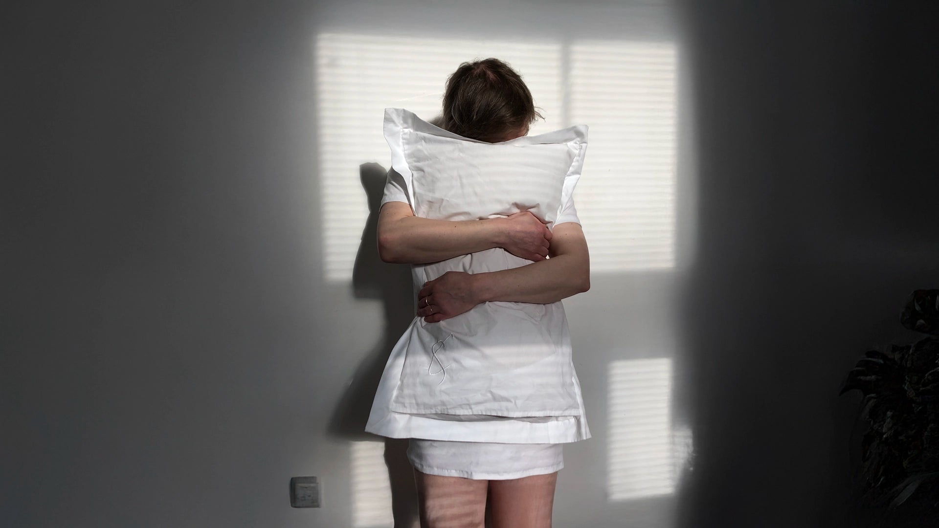A person clutches a white pillow to their chest in soft window light, evoking the emotional care and connection at the heart of Cunnington & Sanderson's Cherish ethos.