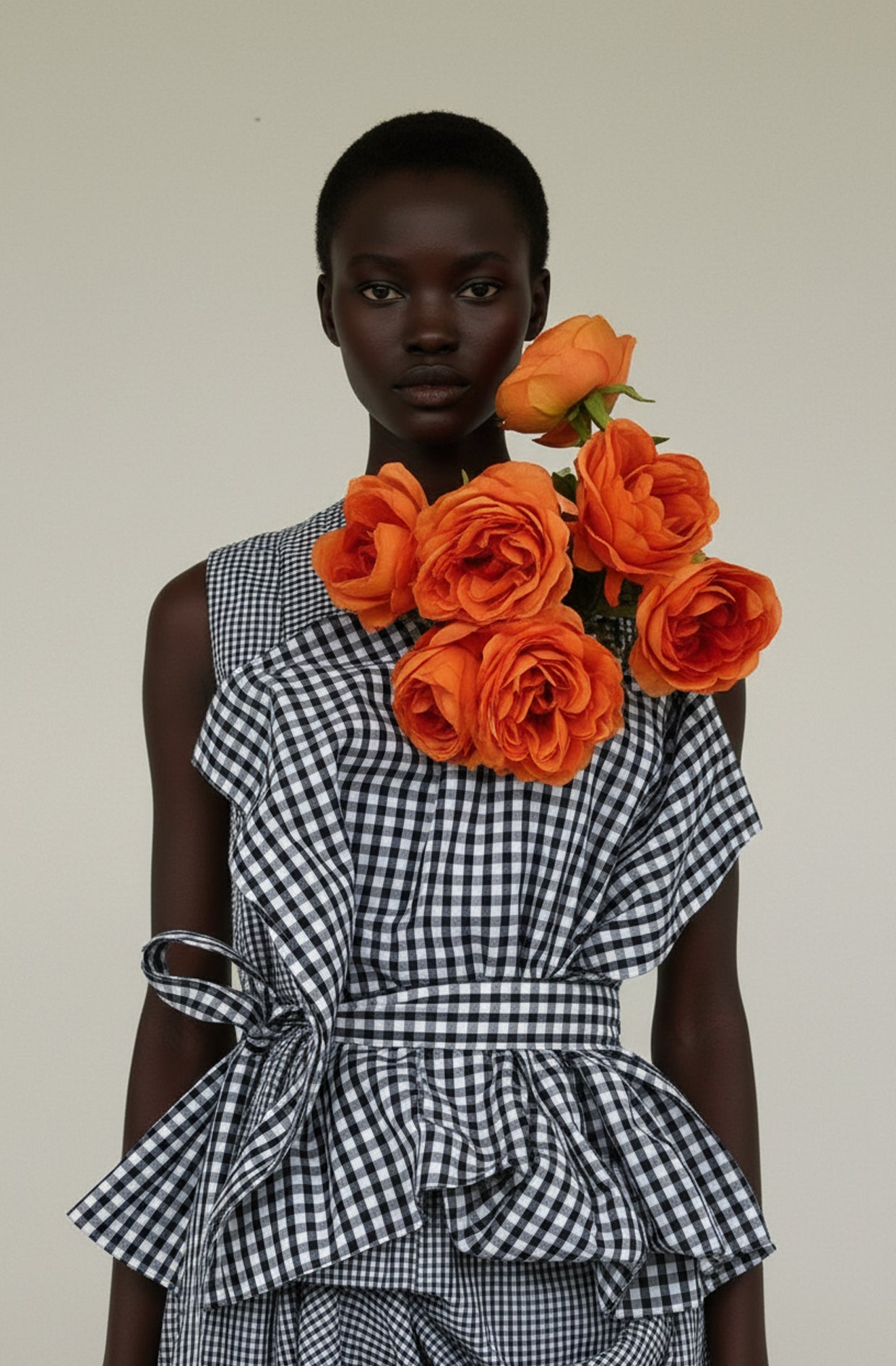 Model wearing a black and white Gginham dress with orange roses on a plain background