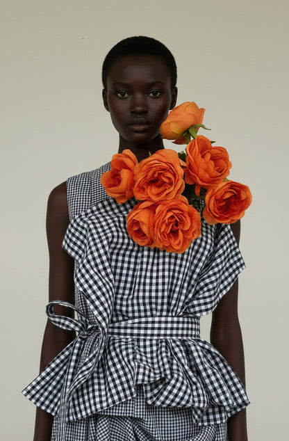 Model wearing a black and white Gginham dress with orange roses on a plain background
