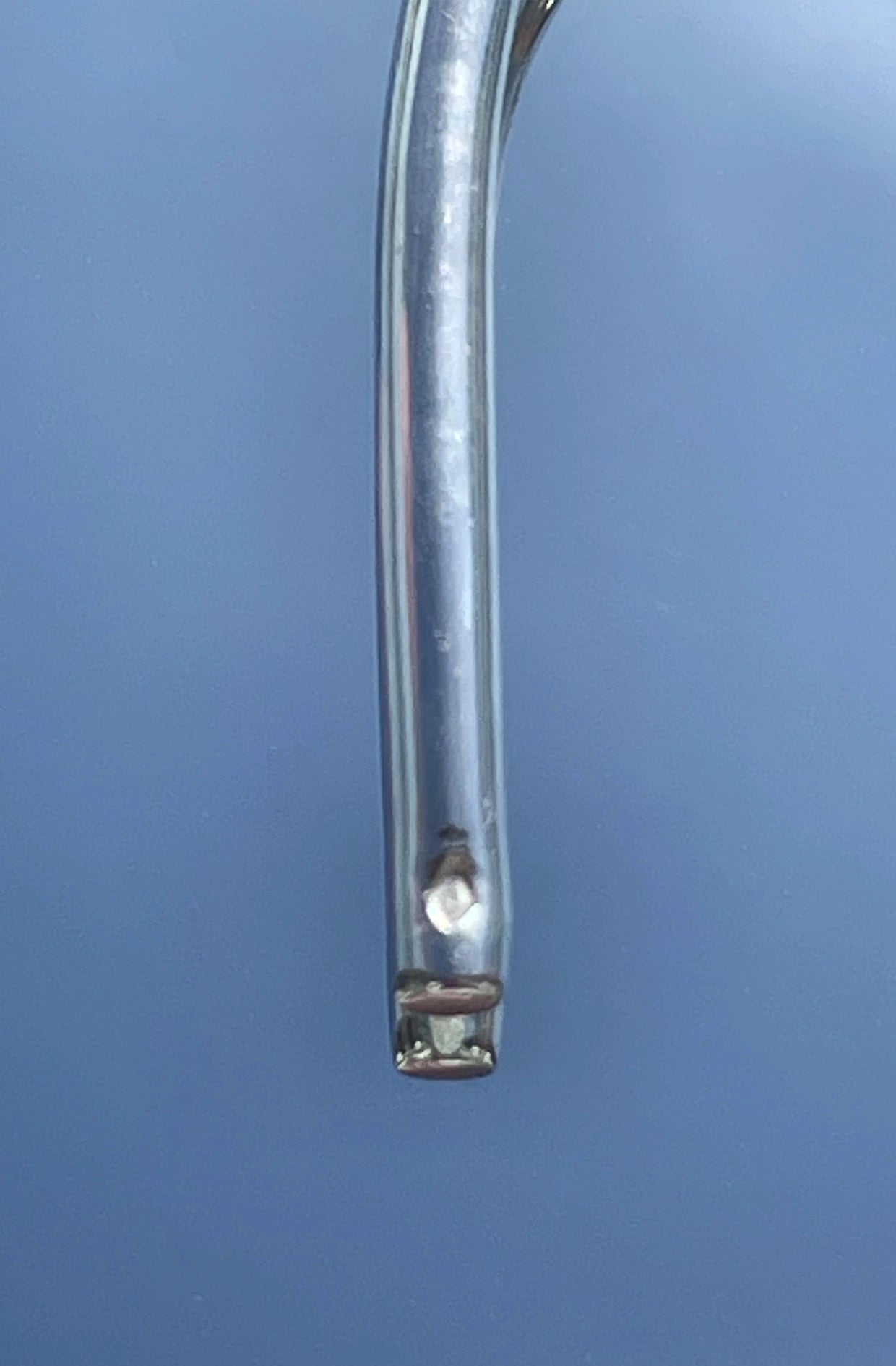 Metallic silver earing object with a central cylindrical component on a blue background with hallmark stamp