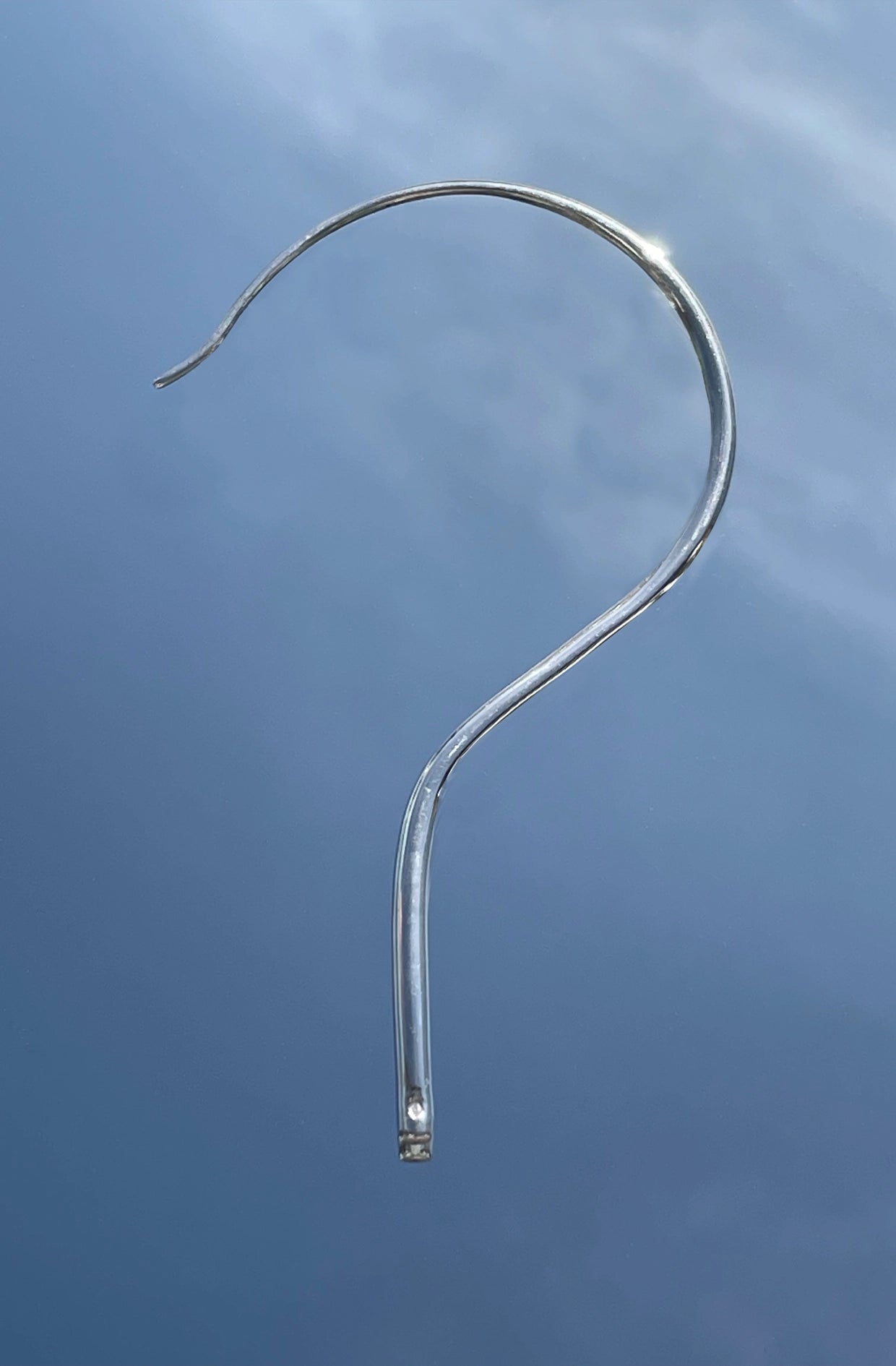 Metallic silver question mark unisex earing against a blue sky made in Paris