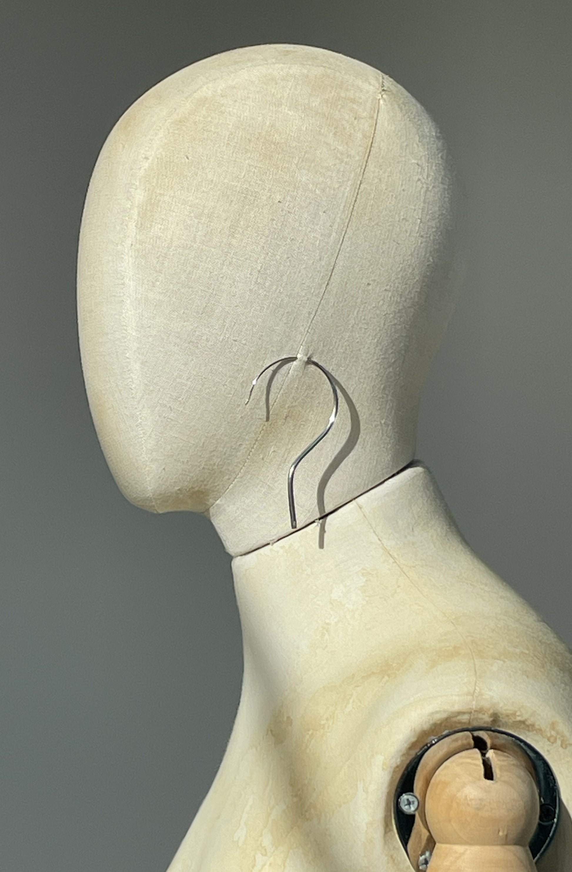 Close-up of a wooden mannequin head with a unisex question mark silver earring 