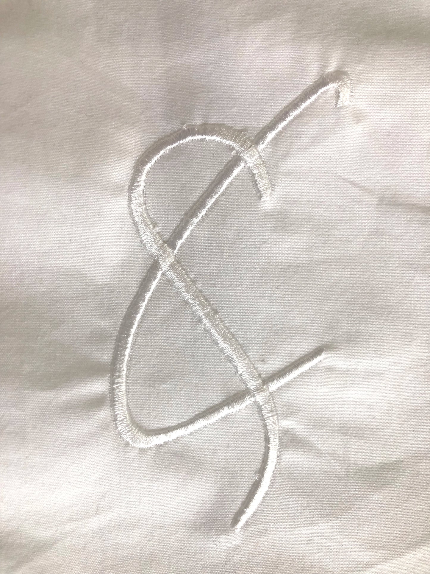 White embroidered Cunnington & Sanderson logo letter c & s on a organic cotton fabric background