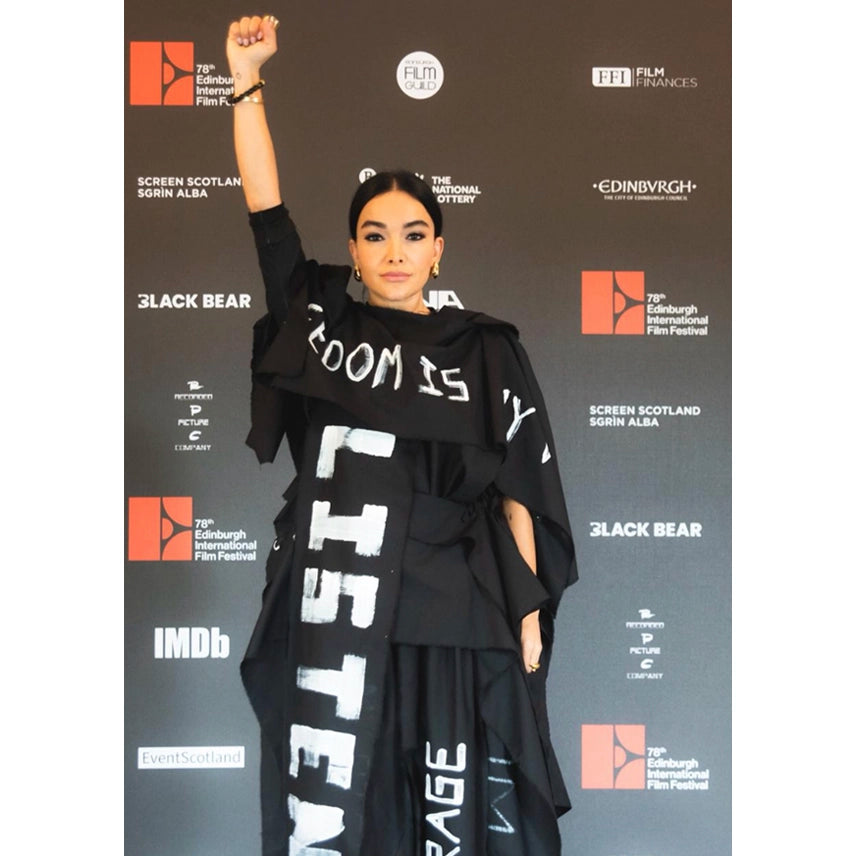 Singer and actree Gola wearing a black outfit with white text called the ballad dress, made with banners in protest, standing against a backdrop with festival logos.