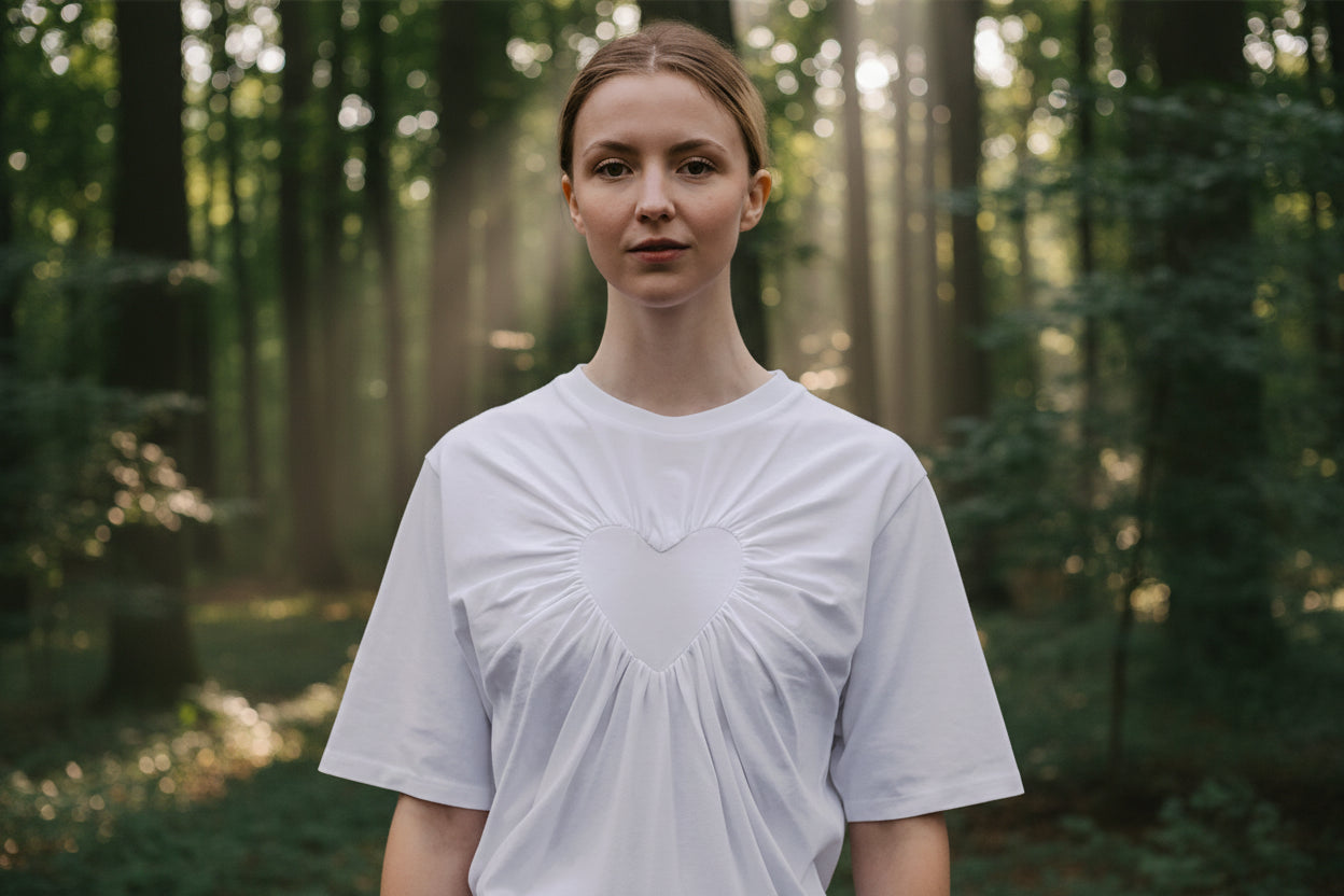 Female model wearing a white t-shirt with a gathered heart design against a brown background