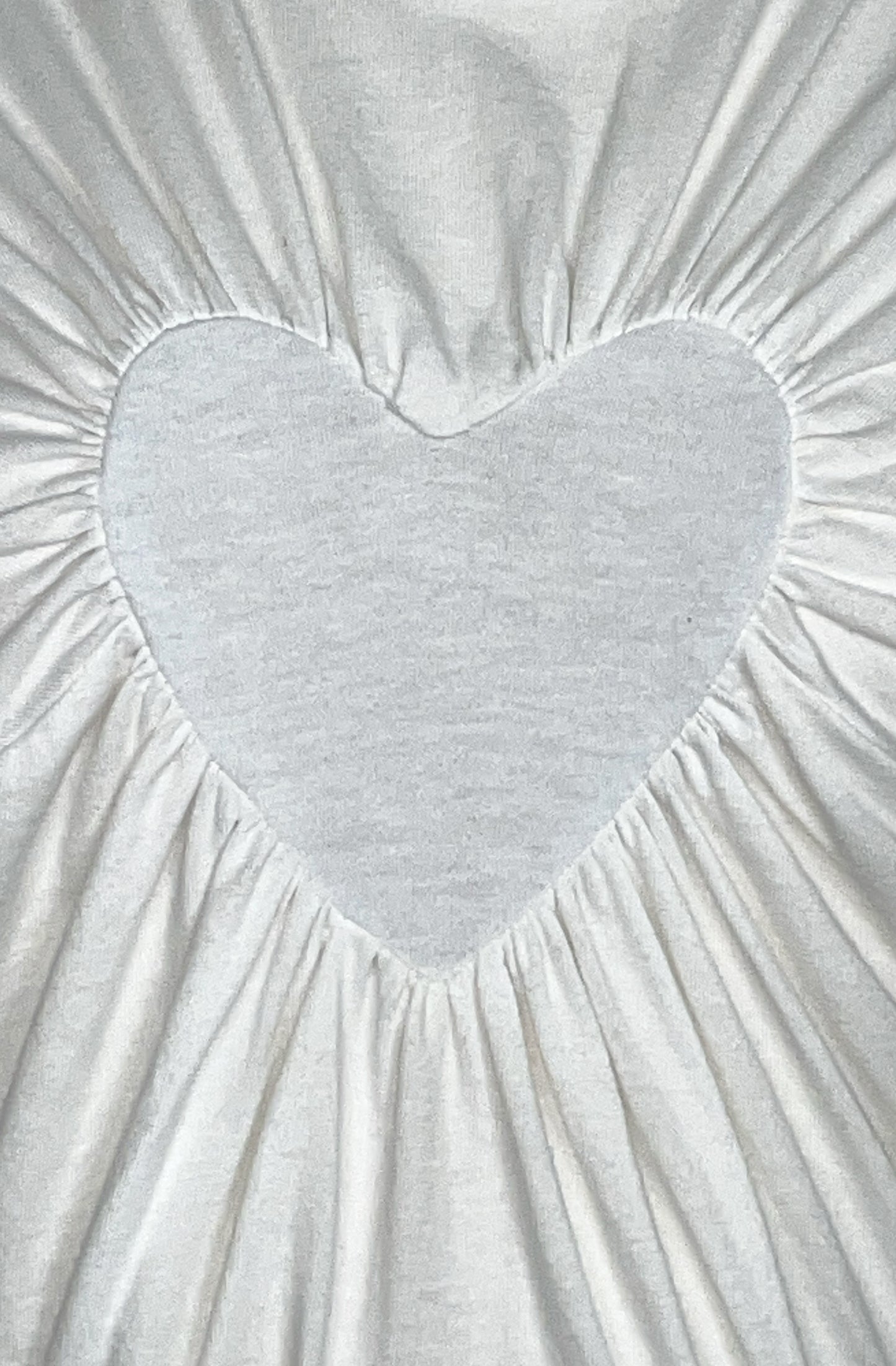 Gathered heart-shaped detail on a textured white organic cotton fabric t-shirt background
