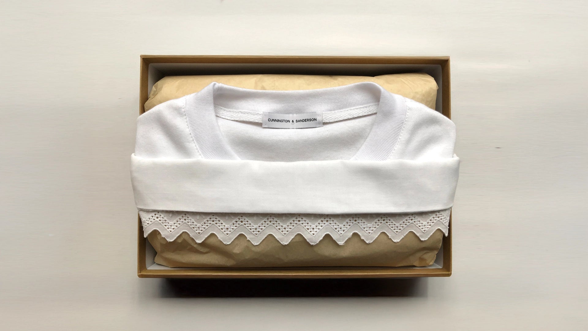 A folded white Cunnington & Sanderson pillow t-shirt garment folded in a eco friendly gift box with recycled tissue paper, showcasing the brand's considered and sustainable packaging.