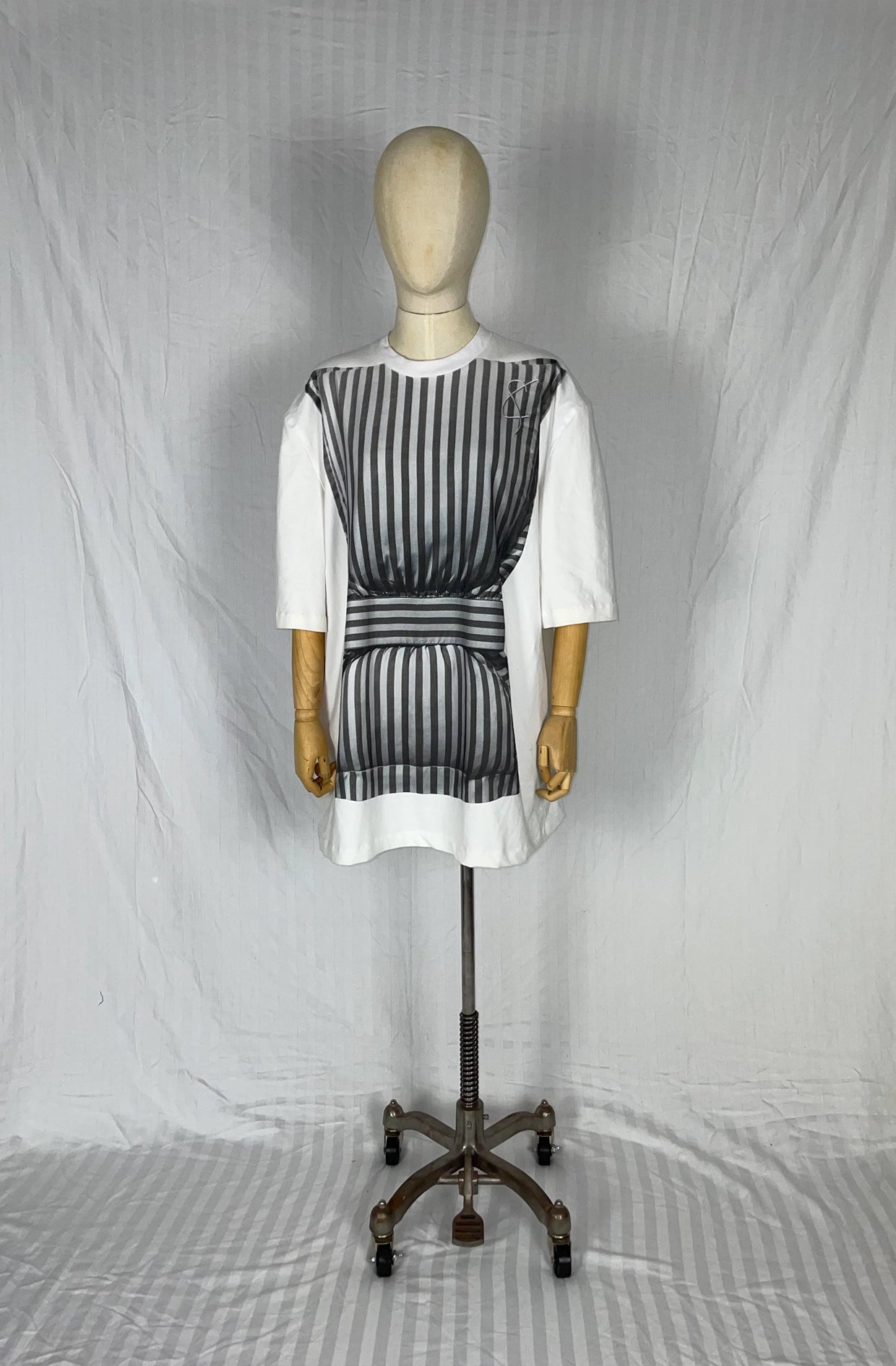 Mannequin wearing a white dress top with a grey striped pillow against a plain background