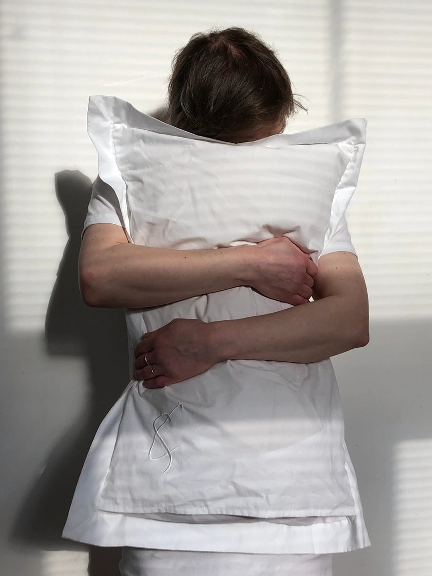 Person wearing a white pillow t-shirt outfit holding a pillow