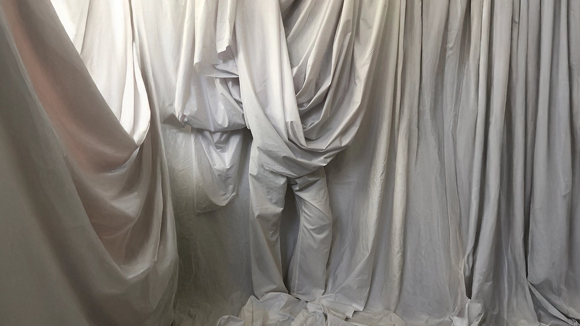 Lengths of pale grey fabric draped and gathered to form a human silhouette, evoking the craftsmanship and human care behind the Cunnington & Sanderson supply chain.