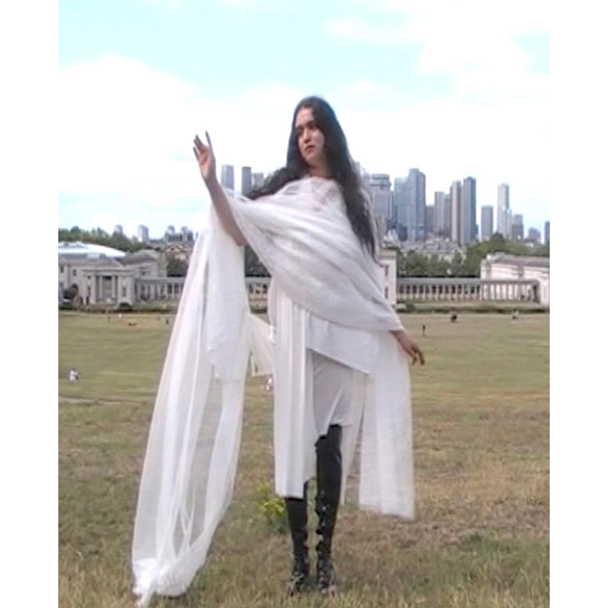 Actress in a white curtain dress with a long train standing in a grassy field in London with a city skyline in the background