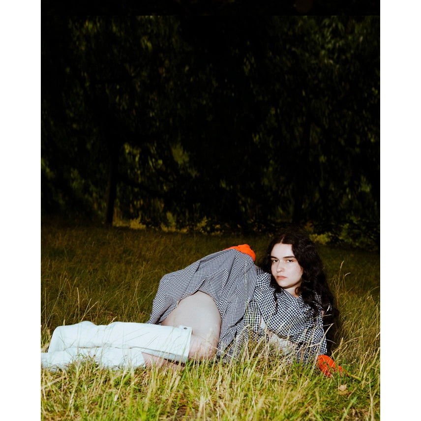 Actres model lying on grass with a checkered blanket top and gingham chandelier skirt and red gloves